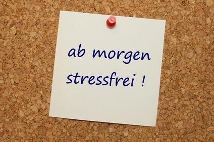 Weiße quadratische Notiz mit blauer Handschrift „ab morgen stressfrei!“ an einer Korktafel befestigt mit einer roten Stecknadel.